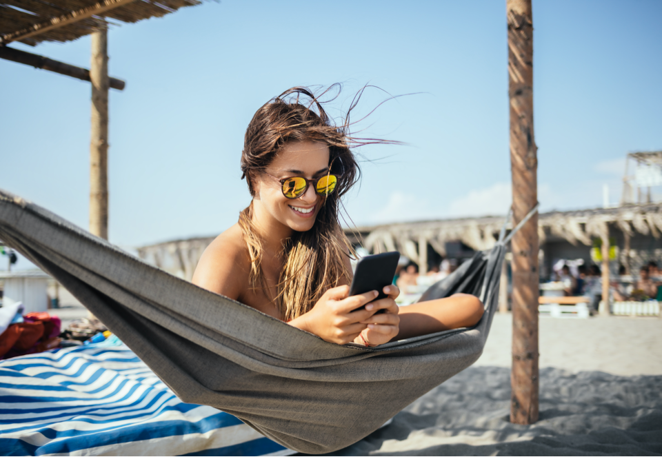 Woman on the beach in a hammock smiling at her phone