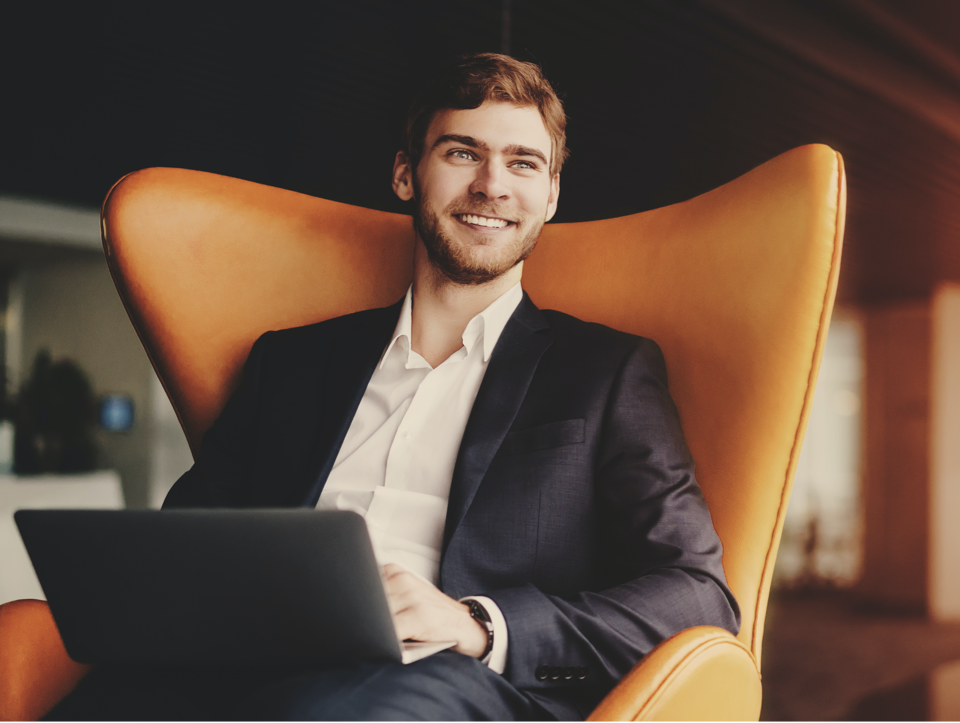 Man with laptop smiling while sitting on armchair